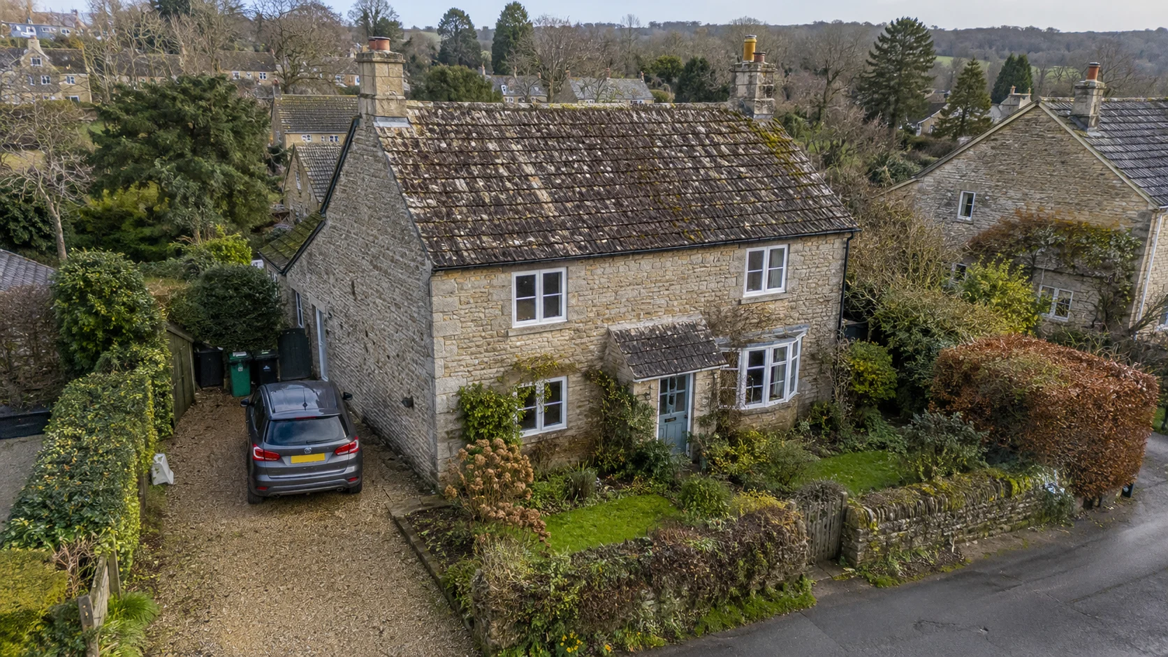 Low aerial view of a cottage, garden and driveway